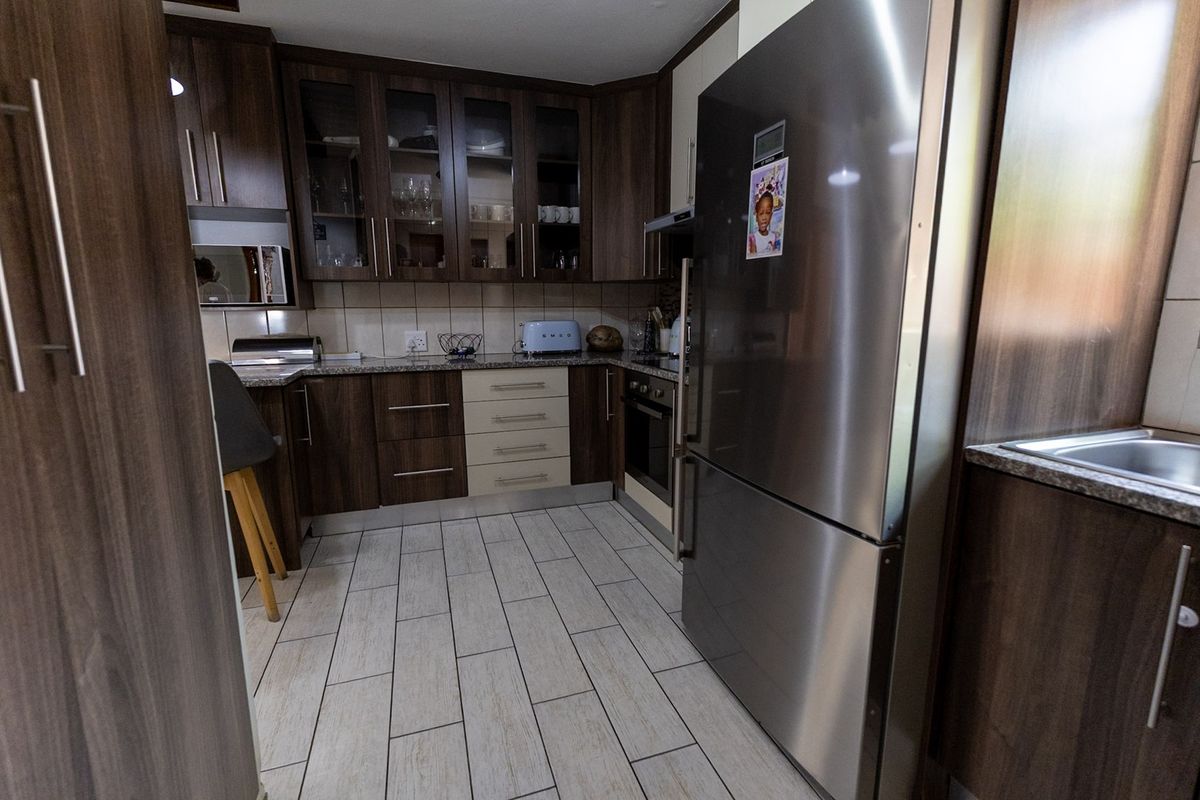 A modern kitchen featuring dark wood cabinetry, granite countertops, tiled flooring, and integrated appliances, offering a functional and well-maintained cooking space.