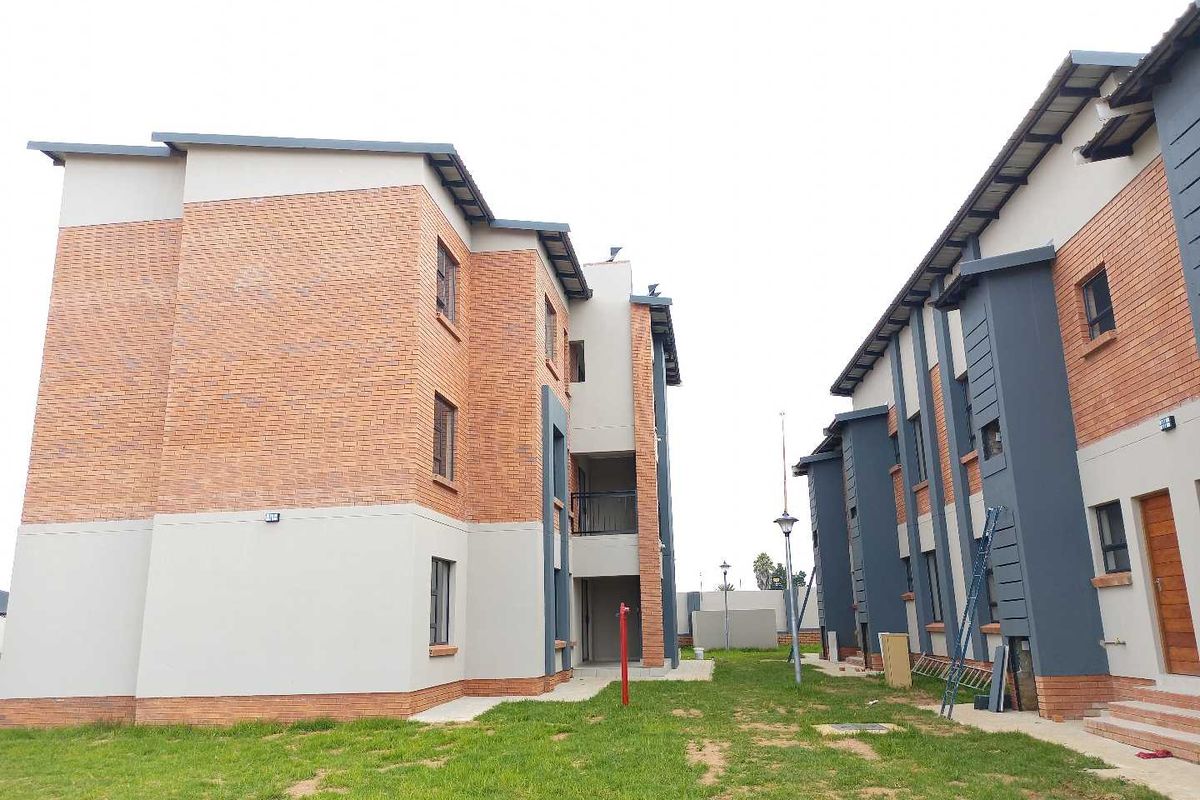Exterior view of a modern townhouse complex featuring face brick and rendered facades with paved walkways and communal garden areas.