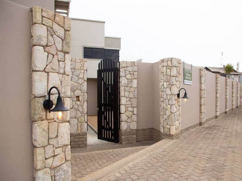 A well-maintained front entrance featuring stone-clad pillars, a secure pedestrian gate, and modern exterior lighting along a paved driveway.