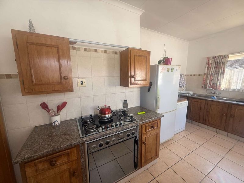 A functional kitchen featuring wooden cabinetry, granite countertops, a gas hob with oven, and tiled flooring, offering a classic layout with ample storage space.