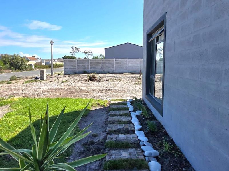 Side view of the property showing the exterior concrete block wall, aluminium window frame, and a landscaped garden path leading to the rear yard.