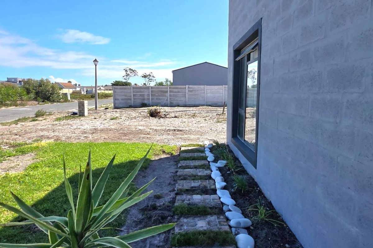 Side view of the property showing the exterior concrete block wall, aluminium window frame, and a landscaped garden path leading to the rear yard.