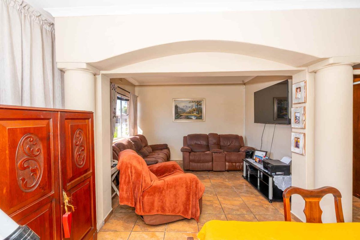 A comfortable living room featuring tiled flooring and a distinct arched architectural opening supported by decorative columns, creating a defined lounge space.