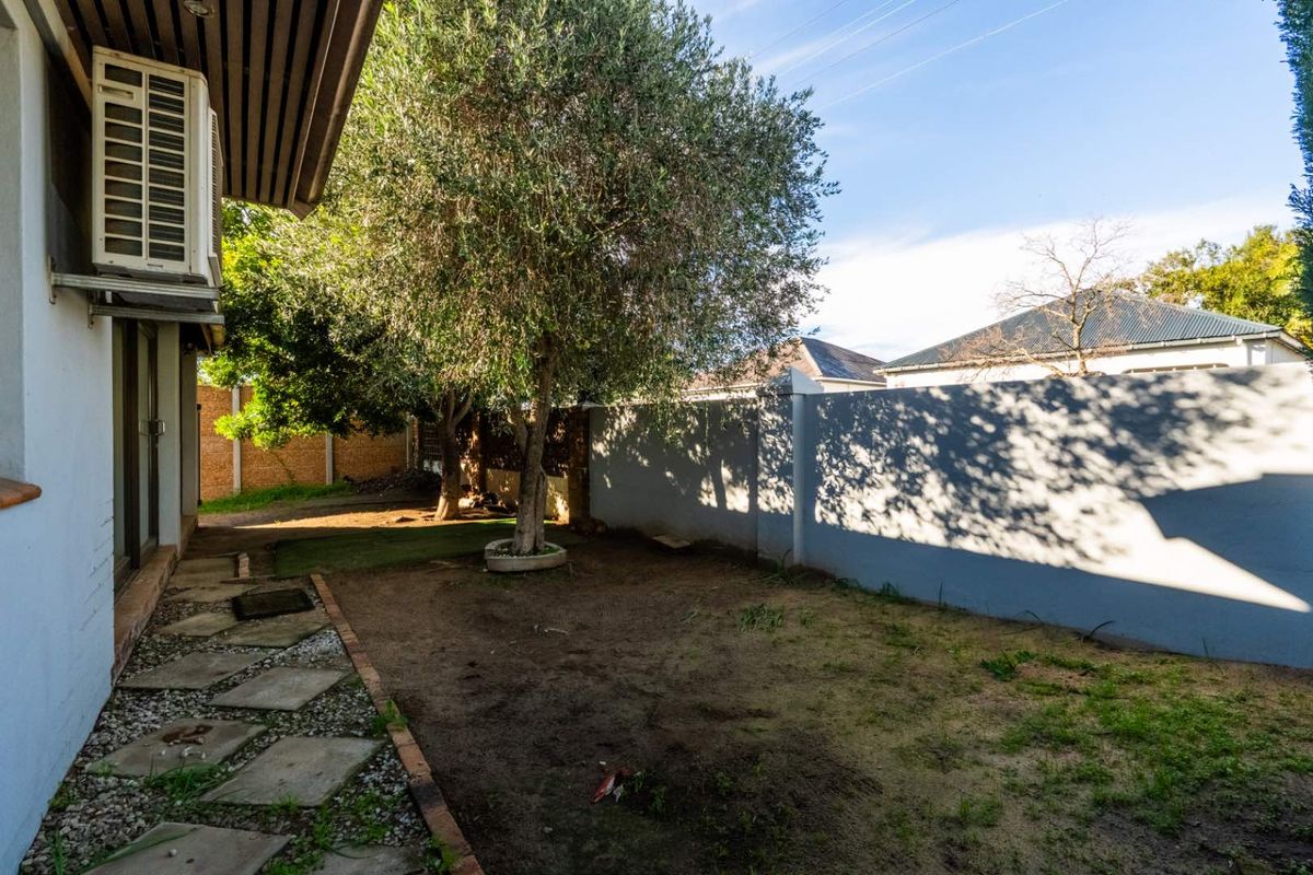 Rear garden area featuring a boundary wall, paved walkway, and established trees, offering potential for landscaping and outdoor improvement.