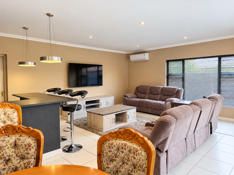 Spacious open-plan living area featuring tiled flooring, a breakfast bar with pendant lighting, and a wall-mounted air conditioning unit.