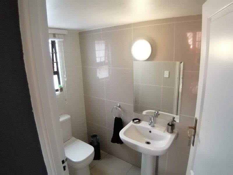 A clean, modern bathroom featuring a pedestal basin, wall-mounted mirror, and neutral wall tiling.