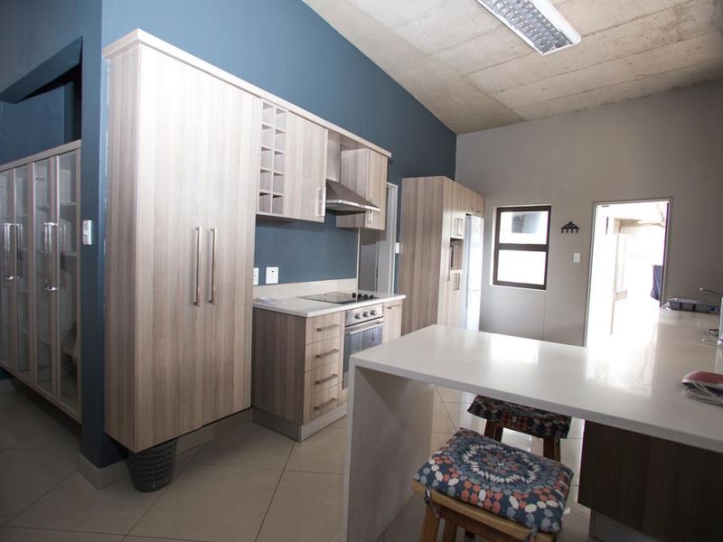 Modern kitchen featuring light wood cabinetry, stone countertops, integrated appliances, and an exposed concrete ceiling, creating a contemporary and functional culinary space.