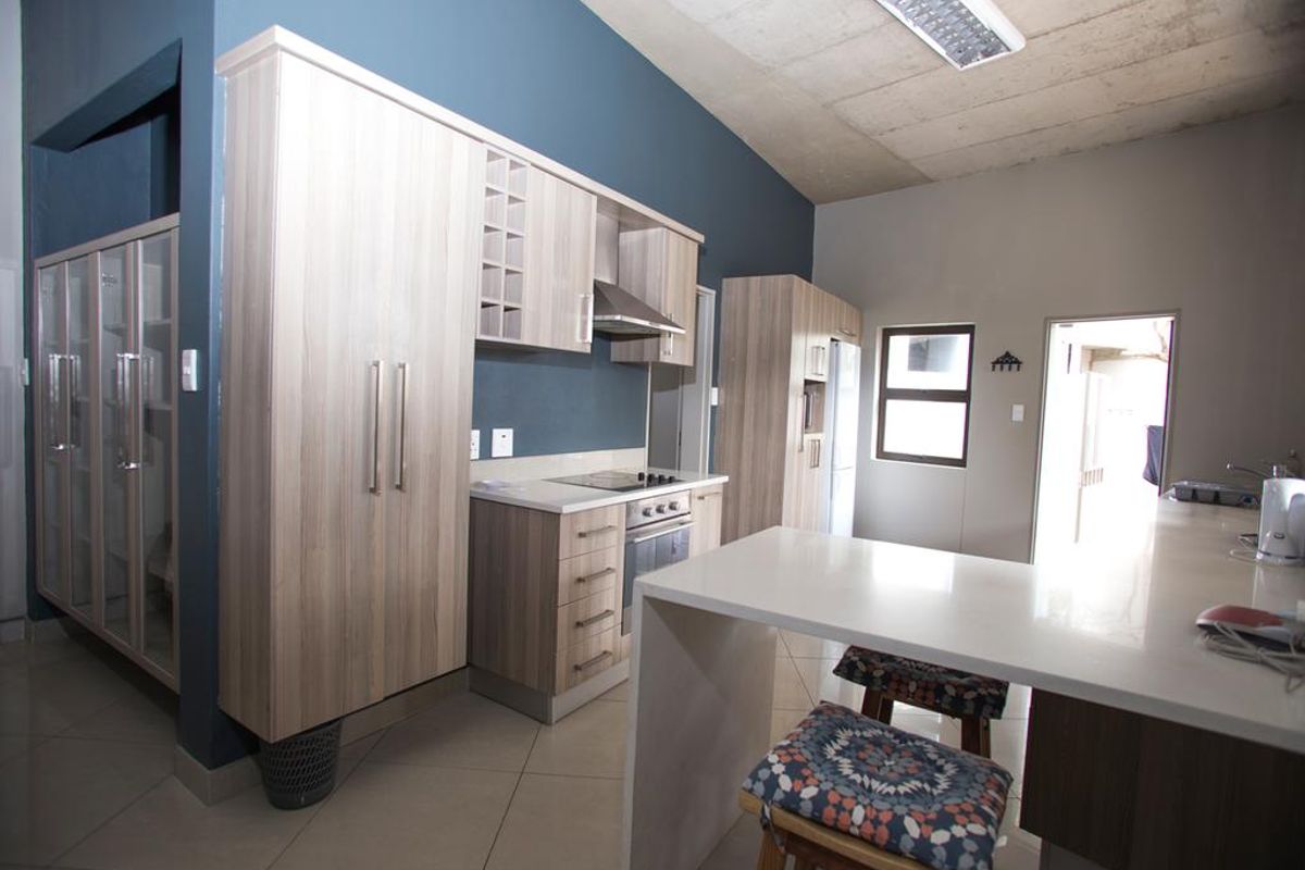 Modern kitchen featuring light wood cabinetry, stone countertops, integrated appliances, and an exposed concrete ceiling, creating a contemporary and functional culinary space.