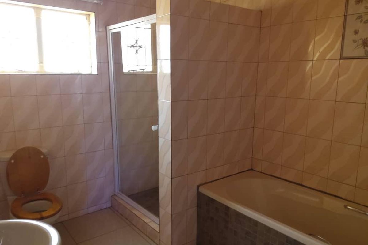 A functional bathroom featuring a built-in bathtub, a separate glass-enclosed shower, and full-height wall tiling.