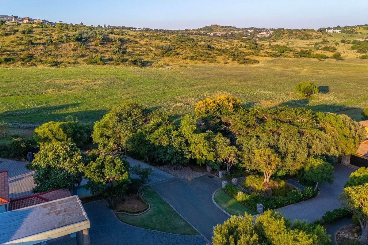 Aerial view of the property grounds featuring paved driveways, mature trees, landscaped garden areas, and expansive open field views.