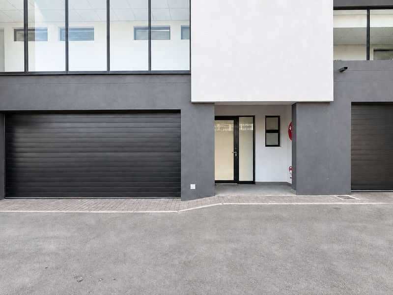 Modern apartment exterior featuring a clean facade, double garage doors, and a glass-paneled entrance door with paved driveway access.