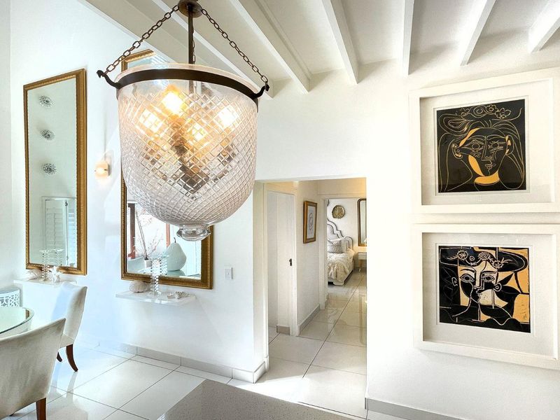 Bright living area featuring exposed ceiling beams, polished tile flooring, and a decorative pendant light, with a view leading into the bedroom.