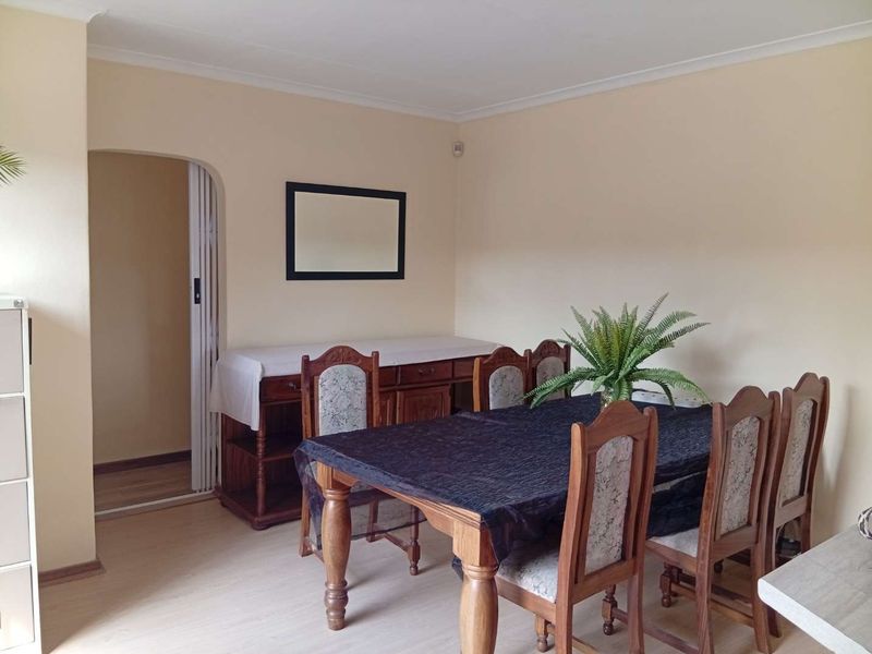 A dining room featuring light-toned laminate flooring and a distinctive arched doorway with a folding door, providing a neutral base for interior updates.