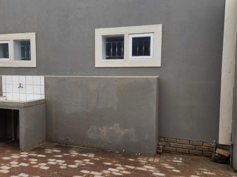 Rear exterior area featuring a concrete wash basin, tiled splashback, and paved courtyard with security-fitted windows.