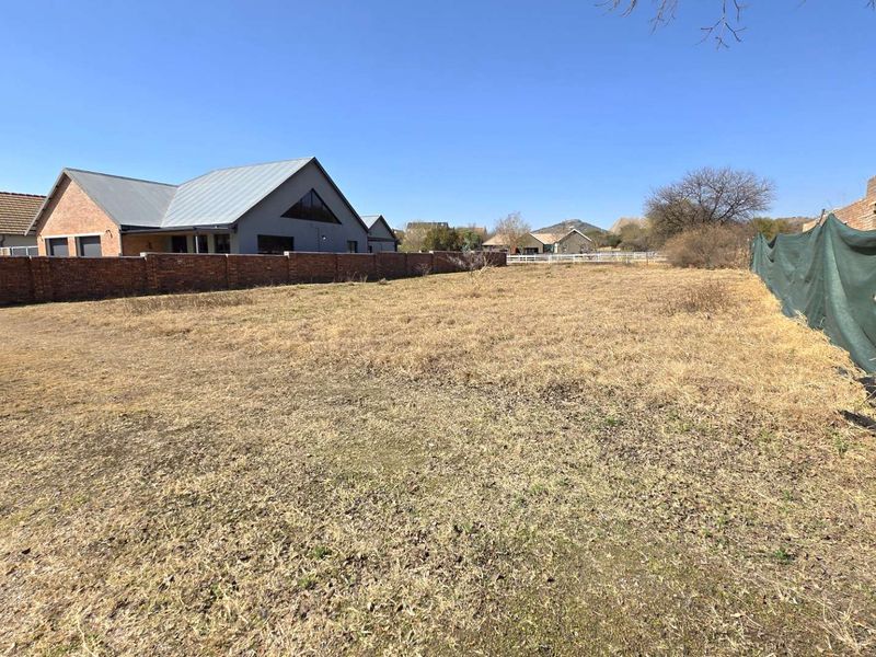 A vacant residential plot featuring dry grass, enclosed by a brick boundary wall and temporary shade cloth fencing.