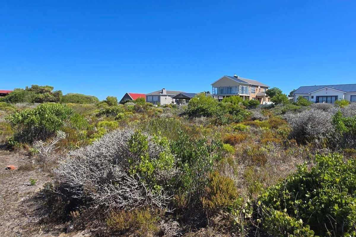 A vacant residential plot featuring natural coastal vegetation with established neighboring properties in the background.