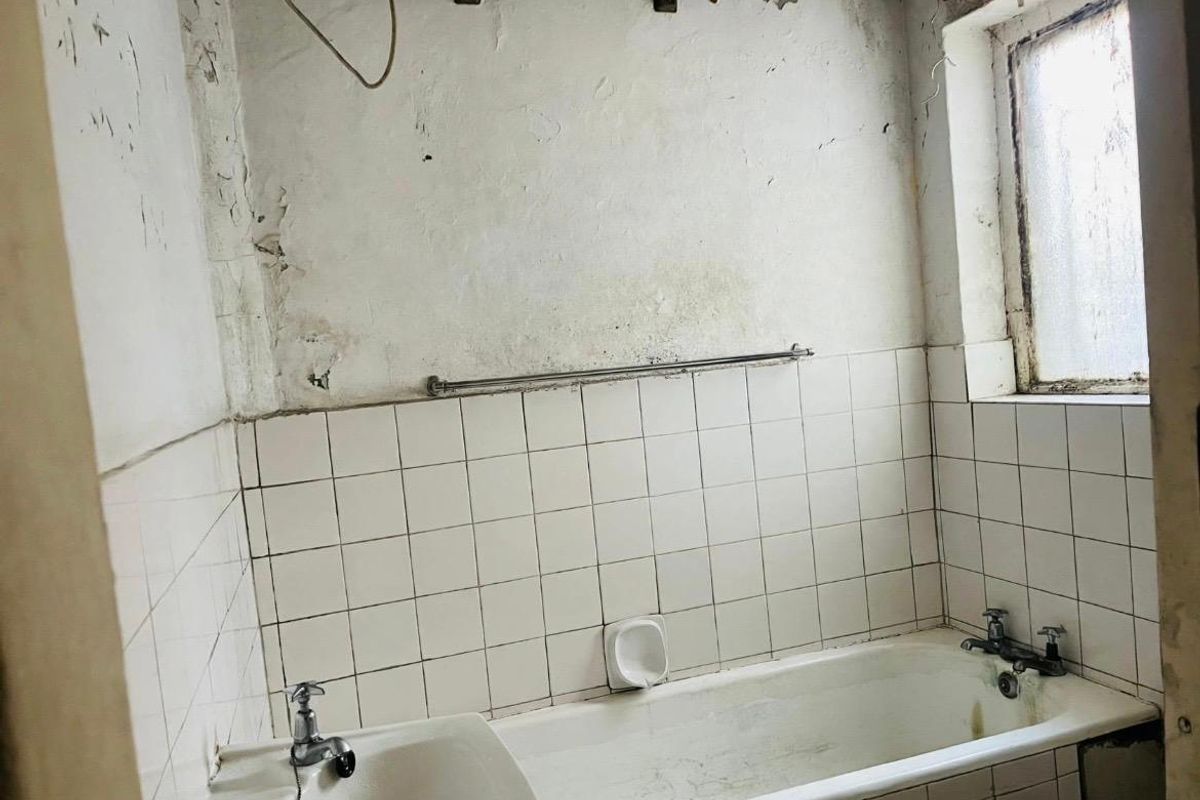 A dated bathroom requiring significant renovation, featuring a standard bathtub, tiled splashback, and visible wall surface deterioration.