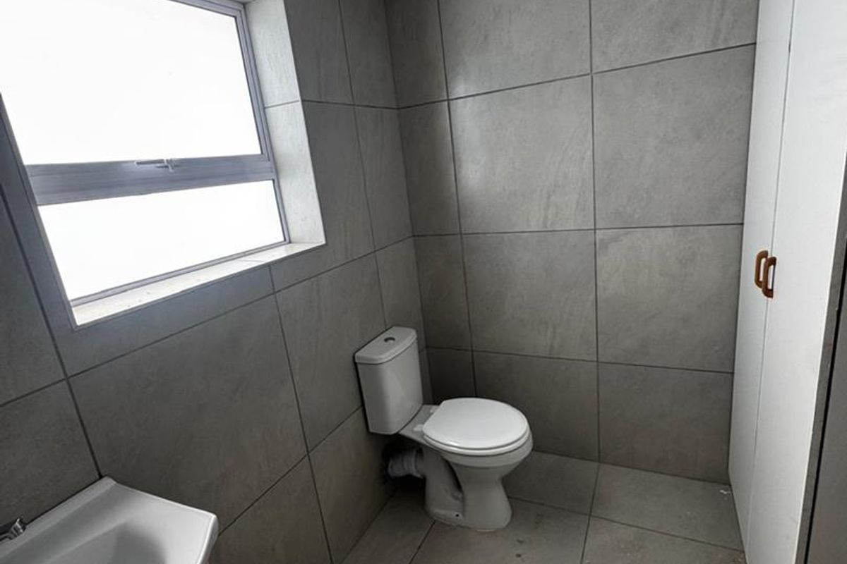 A modern bathroom featuring large-format grey wall and floor tiles, a white toilet, a vanity basin, and built-in storage cabinetry.