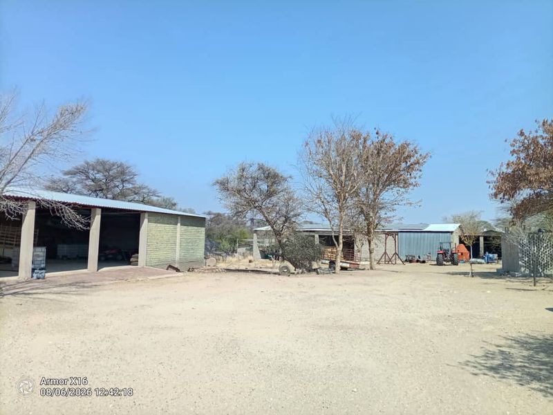 A spacious outdoor yard area featuring multiple open-sided agricultural structures and barns with corrugated metal roofing on a small holding property.