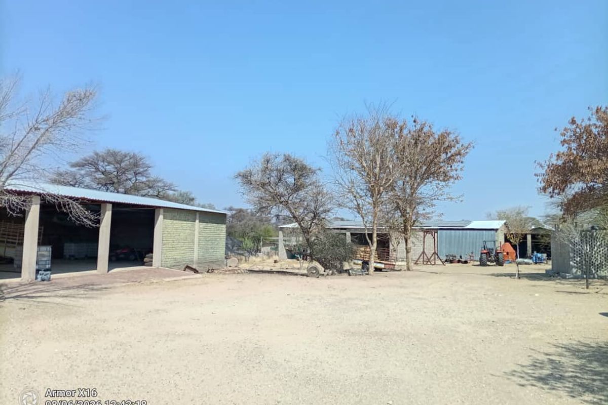 A spacious outdoor yard area featuring multiple open-sided agricultural structures and barns with corrugated metal roofing on a small holding property.