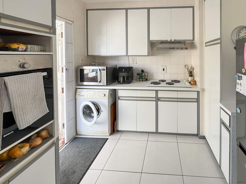 Compact kitchen featuring built-in cabinetry, electric hob, oven, extractor fan, and integrated laundry space with tiled flooring and backsplash.