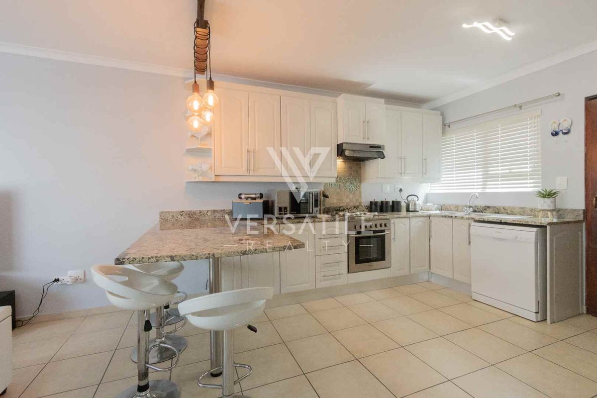 Modern kitchen featuring white cabinetry, granite countertops, a breakfast bar, built-in oven, extractor fan, and tiled flooring.