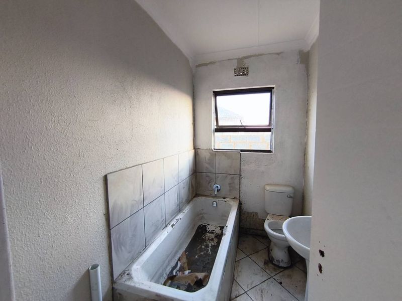 A small, dated bathroom requiring significant renovation, featuring a bathtub, toilet, and pedestal basin with unfinished wall surfaces and worn floor tiles.