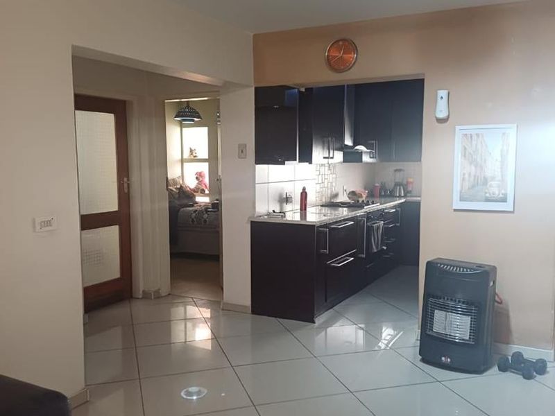 Open plan living area featuring large format floor tiles and a compact kitchen with dark cabinetry, integrated hob, and extractor fan.