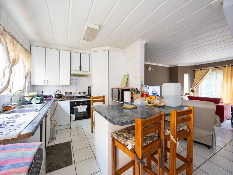 Open-plan kitchen and living area featuring white cabinetry, laminate countertops, gas hob, and tiled flooring, offering a functional layout for daily living.