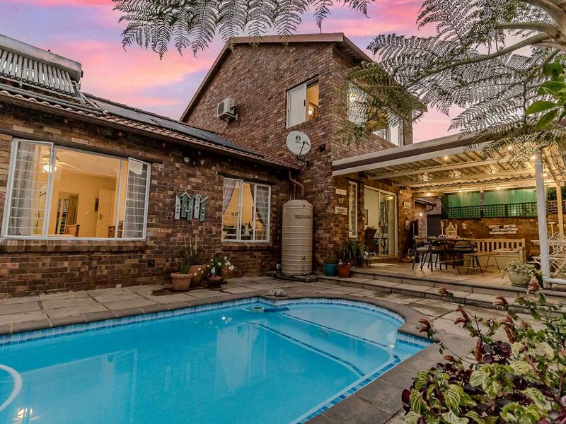A private backyard featuring a swimming pool, a covered patio area, and a multi-story brick townhouse facade with solar water heating.