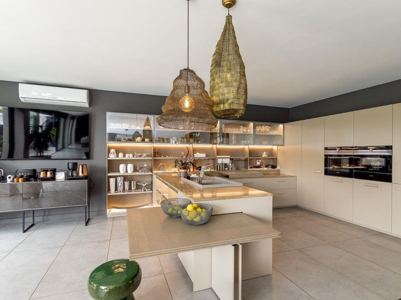 Modern, high-end kitchen featuring a central island, integrated appliances, sleek cabinetry with glass-front displays, and ambient under-cabinet lighting.
