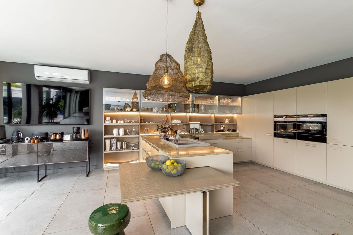 Modern, high-end kitchen featuring a central island, integrated appliances, sleek cabinetry with glass-front displays, and ambient under-cabinet lighting.