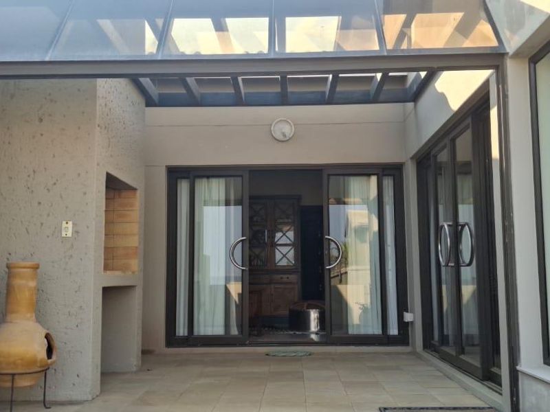 Covered patio area featuring a built-in braai, glass roof canopy, and large aluminium sliding and folding doors providing seamless indoor-outdoor flow.