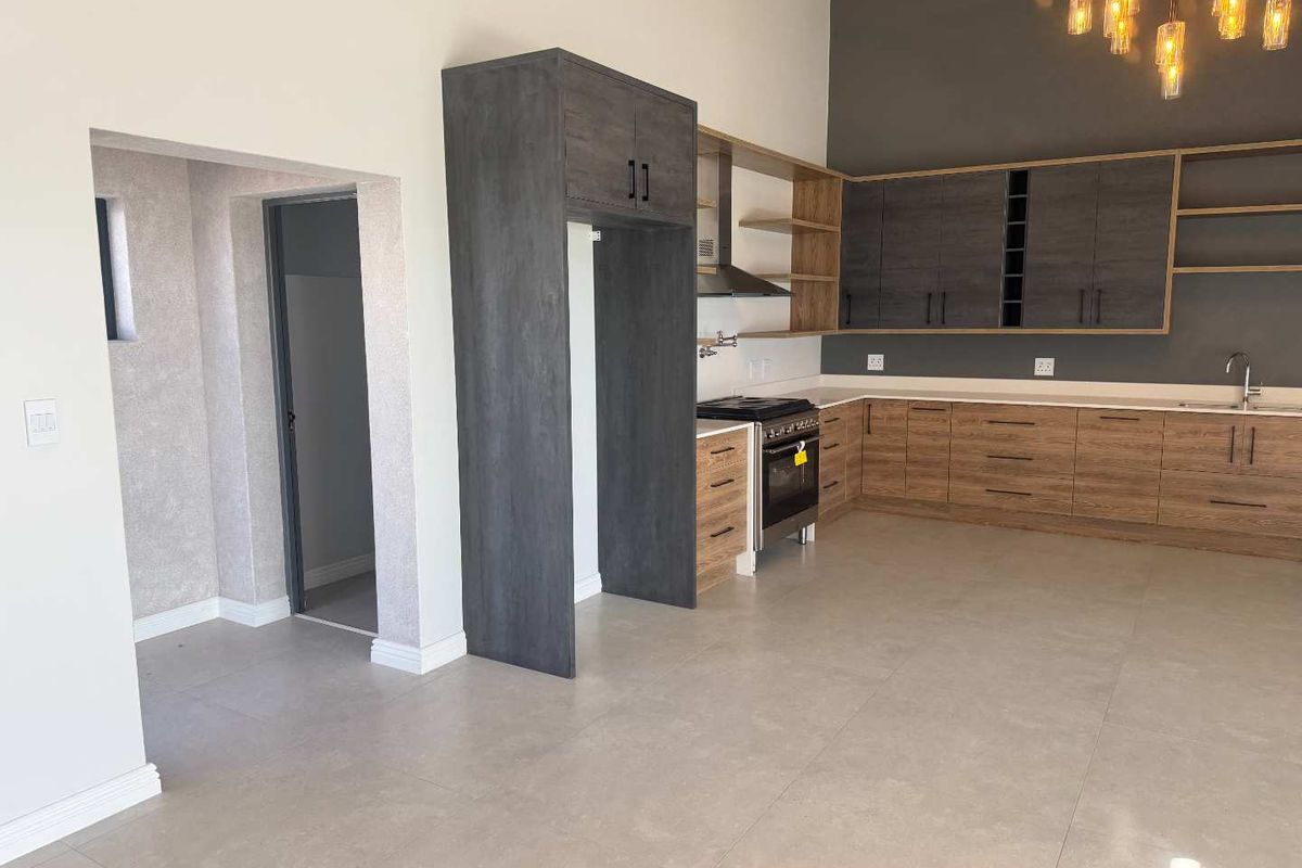 Modern kitchen featuring two-tone cabinetry, built-in oven with extractor fan, stone countertops, and large format floor tiles in an open-plan layout.