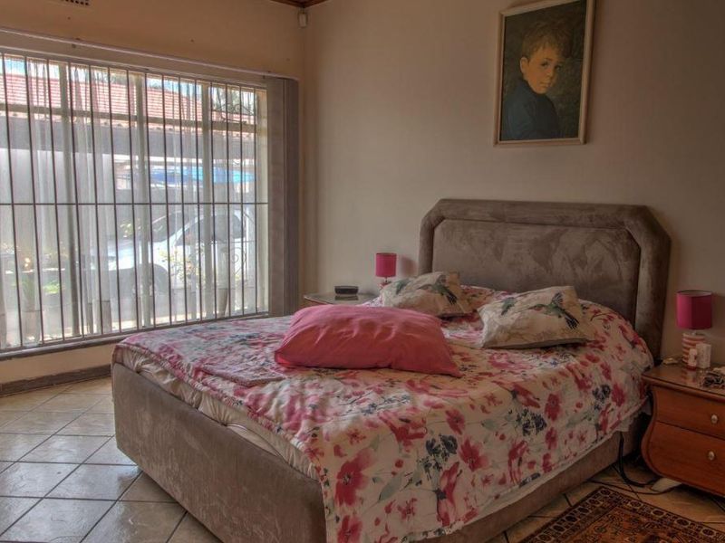 A bedroom featuring tiled flooring and a large window with security bars, providing natural light.