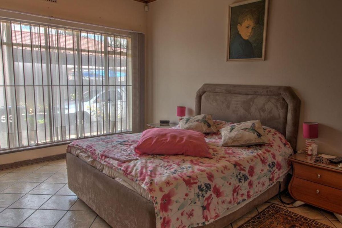 A bedroom featuring tiled flooring and a large window with security bars, providing natural light.