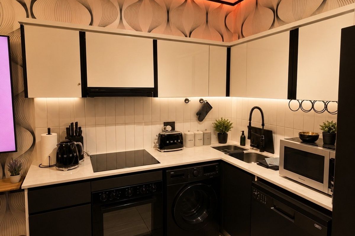 Modern kitchen featuring high-contrast black and white cabinetry, integrated appliances, sleek induction cooktop, and stylish patterned wallpaper with ambient cove lighting.