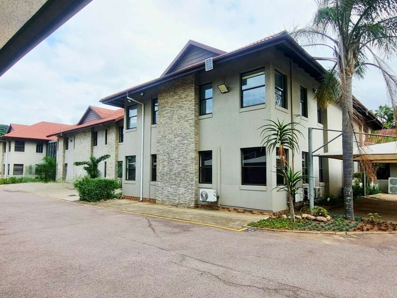 A well-maintained multi-story office building featuring stone cladding accents, tiled roofing, and dedicated paved parking areas with shade cloth carports.