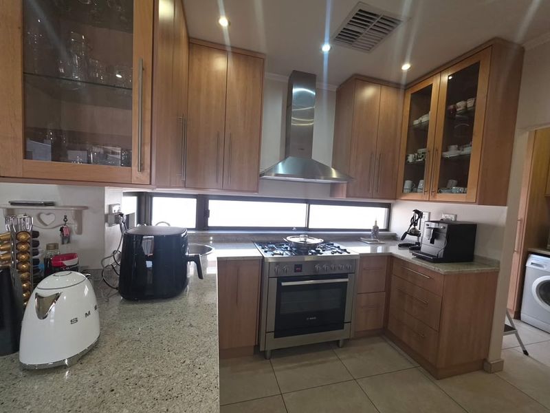 A functional kitchen featuring wooden cabinetry, granite countertops, and a stainless steel gas stove with an extractor fan, complemented by recessed lighting.