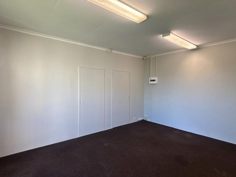 A vacant office space featuring neutral walls, carpeted flooring, and functional overhead fluorescent lighting, suitable for a professional workspace setup.