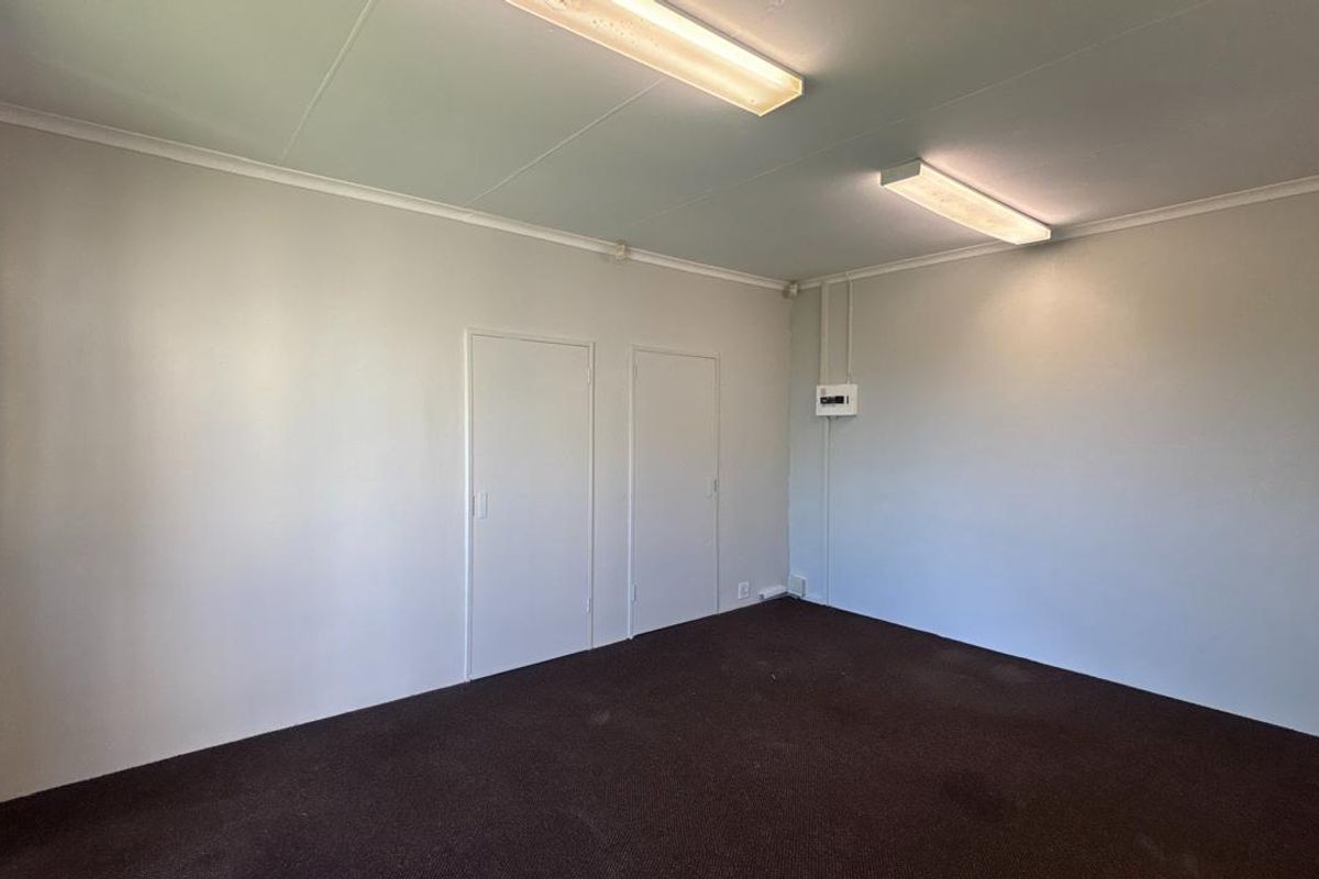 A vacant office space featuring neutral walls, carpeted flooring, and functional overhead fluorescent lighting, suitable for a professional workspace setup.