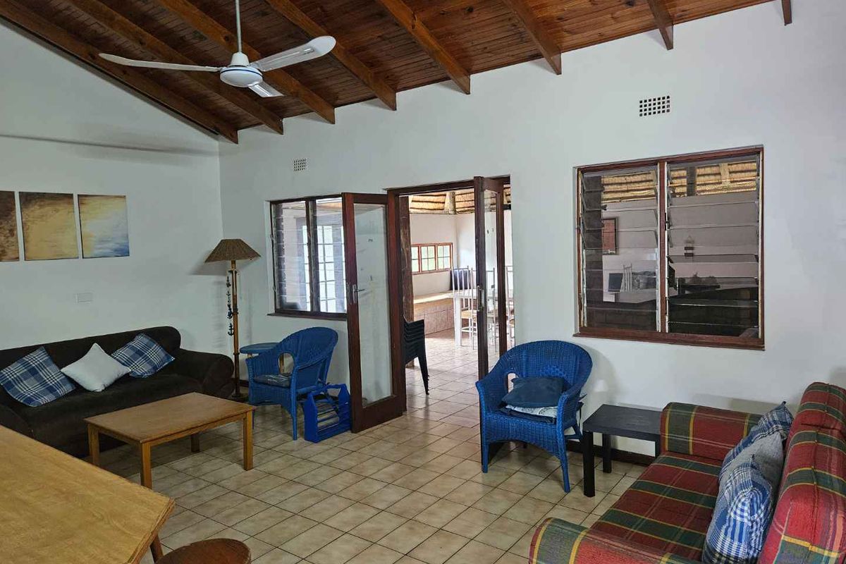 Spacious living area featuring exposed timber beam ceilings, tiled flooring, and direct access to an adjoining room through a wooden door frame.