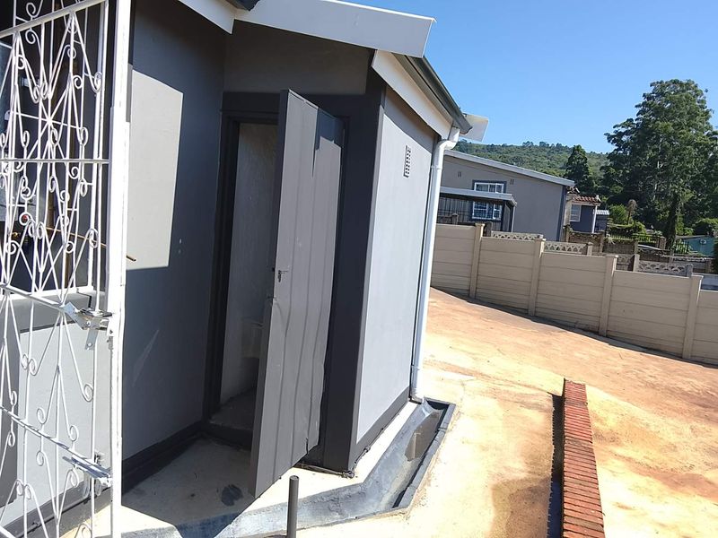 Exterior view of the rear of the property featuring a security gate, concrete paving, and perimeter precast walling.