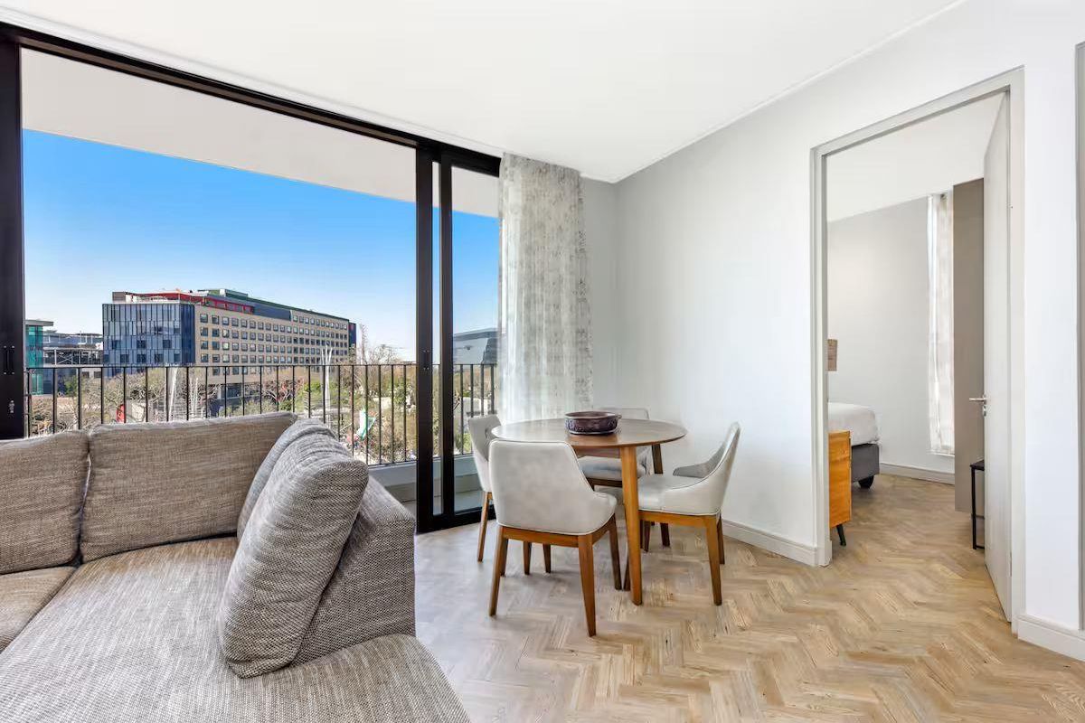 Bright living area featuring herringbone timber flooring and large sliding glass doors opening to a balcony with urban views.