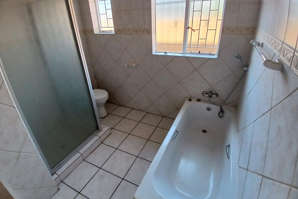 A functional bathroom featuring a bathtub, separate shower enclosure, and toilet, finished with neutral wall and floor tiling.