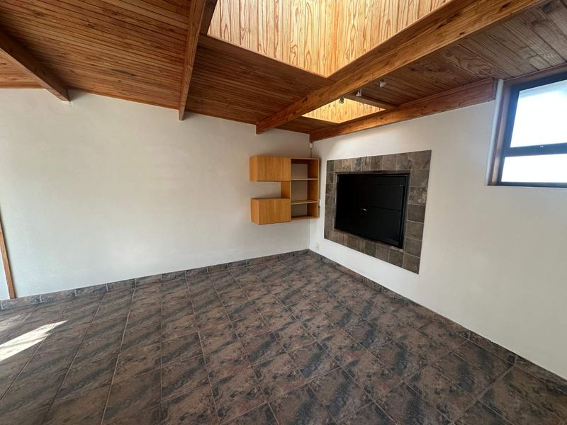 Spacious living room featuring a vaulted timber ceiling with a skylight, tiled flooring, and a built-in fireplace with stone surround.