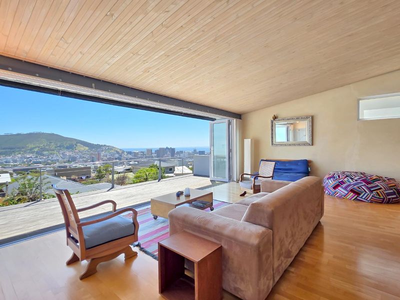 Spacious living area featuring warm timber ceilings, hardwood floors, and expansive sliding doors opening onto a deck with panoramic city and mountain views.