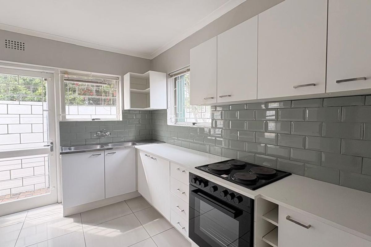 A clean, modern kitchen featuring white cabinetry, a grey subway tile backsplash, built-in oven with electric hob, and direct access to the exterior.