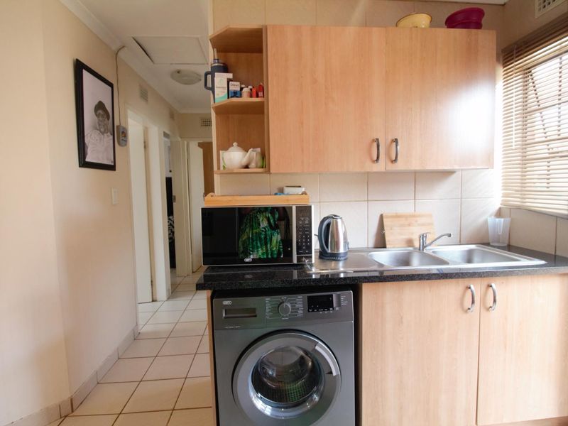 A functional kitchen area featuring light wood cabinetry, granite countertops, a double sink, and tiled flooring, with an integrated space for a washing machine.