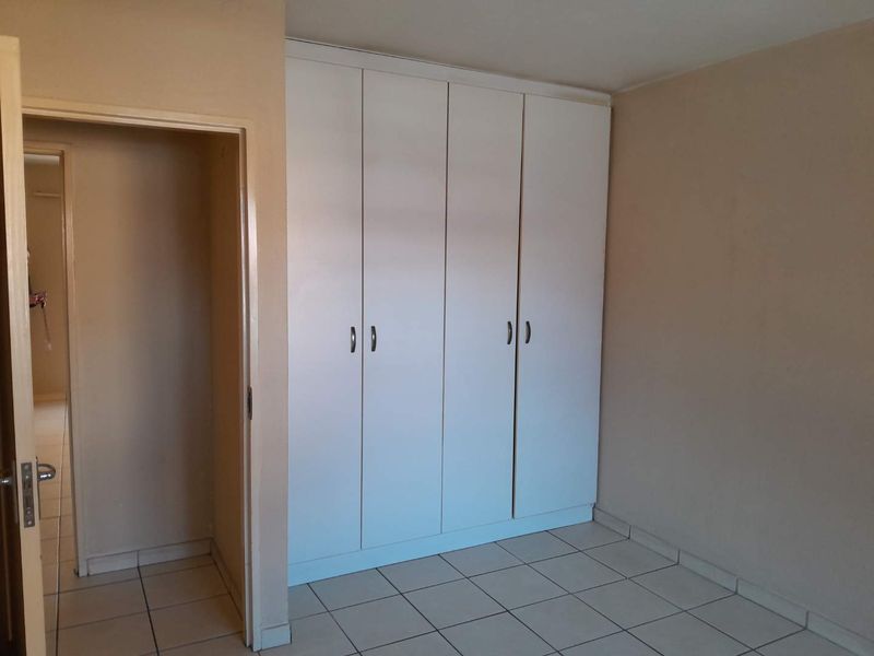 A clean, empty bedroom featuring neutral wall paint, ceramic floor tiles, and white built-in cupboards with modern handles.